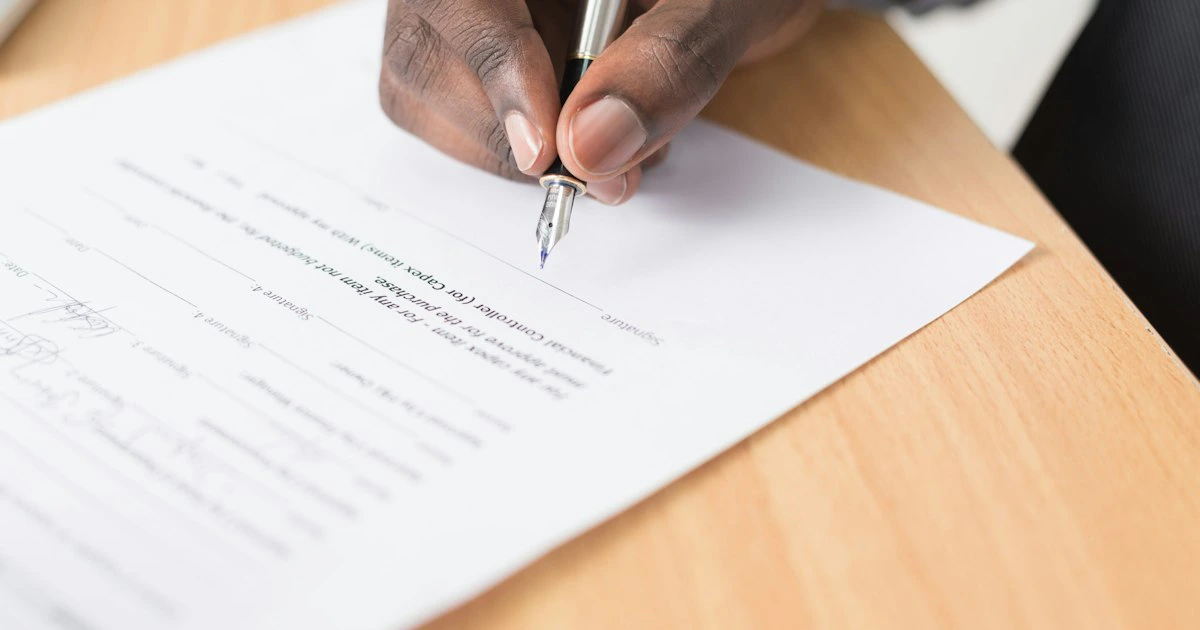 Persona firmando un documento legal con un abogado