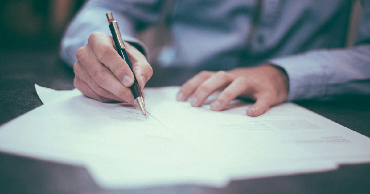 Persona firmando documentos legales en un escritorio de oficina con papeles